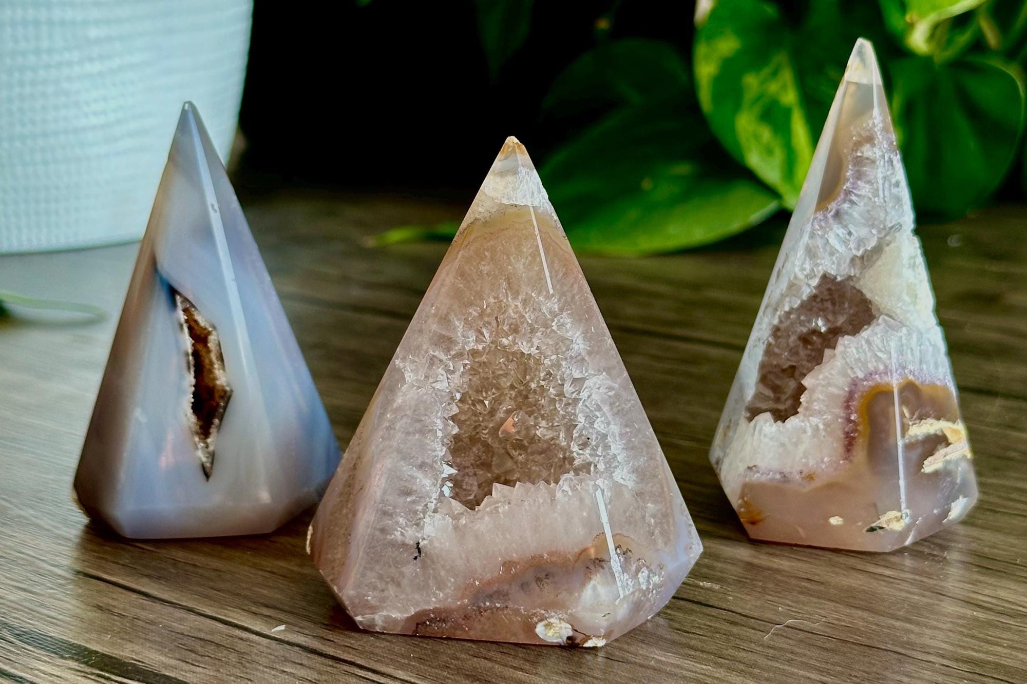 Three triangular crystal stones on a wooden surface with greenery in the background